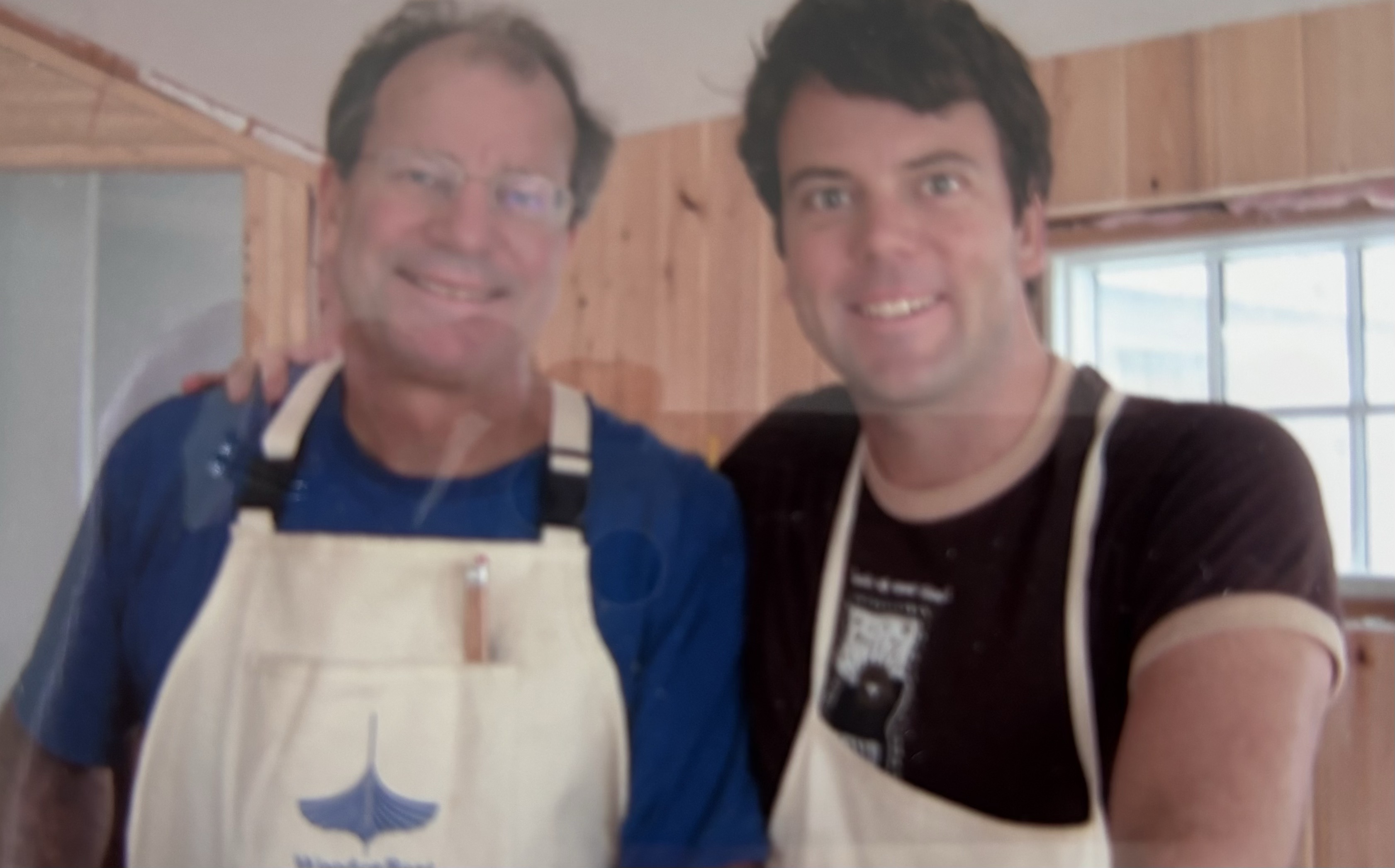 Chris and his dad smiling together in work aprons inside the cottage they were rebuilding.